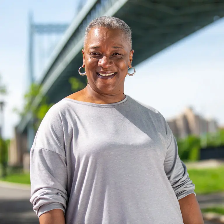 A smiling VNS Health Plans member standing near a bridge.