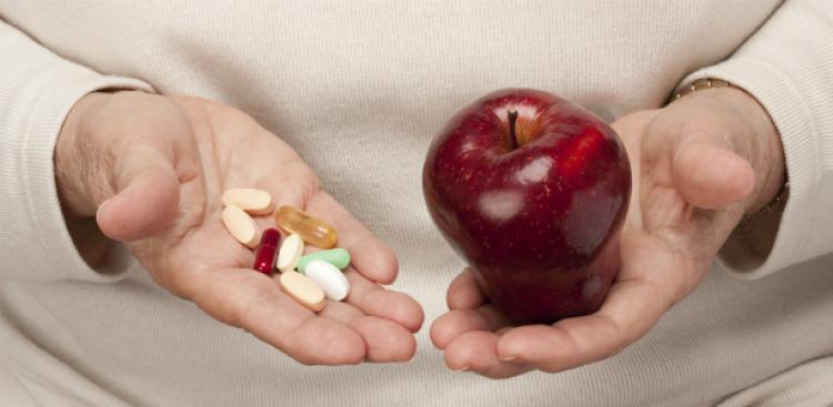 Una persona con vitaminas y suplementos en una mano y una manzana roja en la otra.