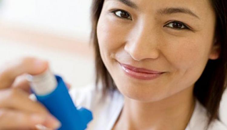 Una mujer sonriente sosteniendo un inhalador para el asma.